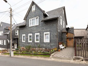 Une maison à deux étages, avec une façade de couleur gris foncé, des encadrements de fenêtres blancs et une porte d’entrée en bois.