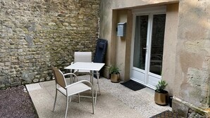 A patio with a table and chairs, a stone wall, a door with glass panels, and a potted plant. - Cottage in Central Bayeux (Bayeux)