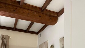 A bedroom with a wooden ceiling, a radiator, a bed with pillows, and wall-mounted artwork. - Cottage in Central Bayeux (Bayeux)