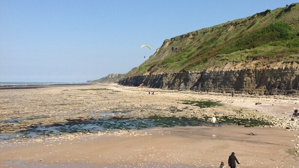 A beach with a cliff, rocky terrain, and a person walking with a child. - Cottage in Central Bayeux (Bayeux)