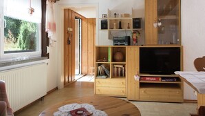 Una sala de estar acogedora con vigas de madera, un ventanal con cortinas, un televisor y una estantería.