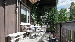 Una terraza de madera con una mesa y sillas blancas, un banco y una planta en maceta.