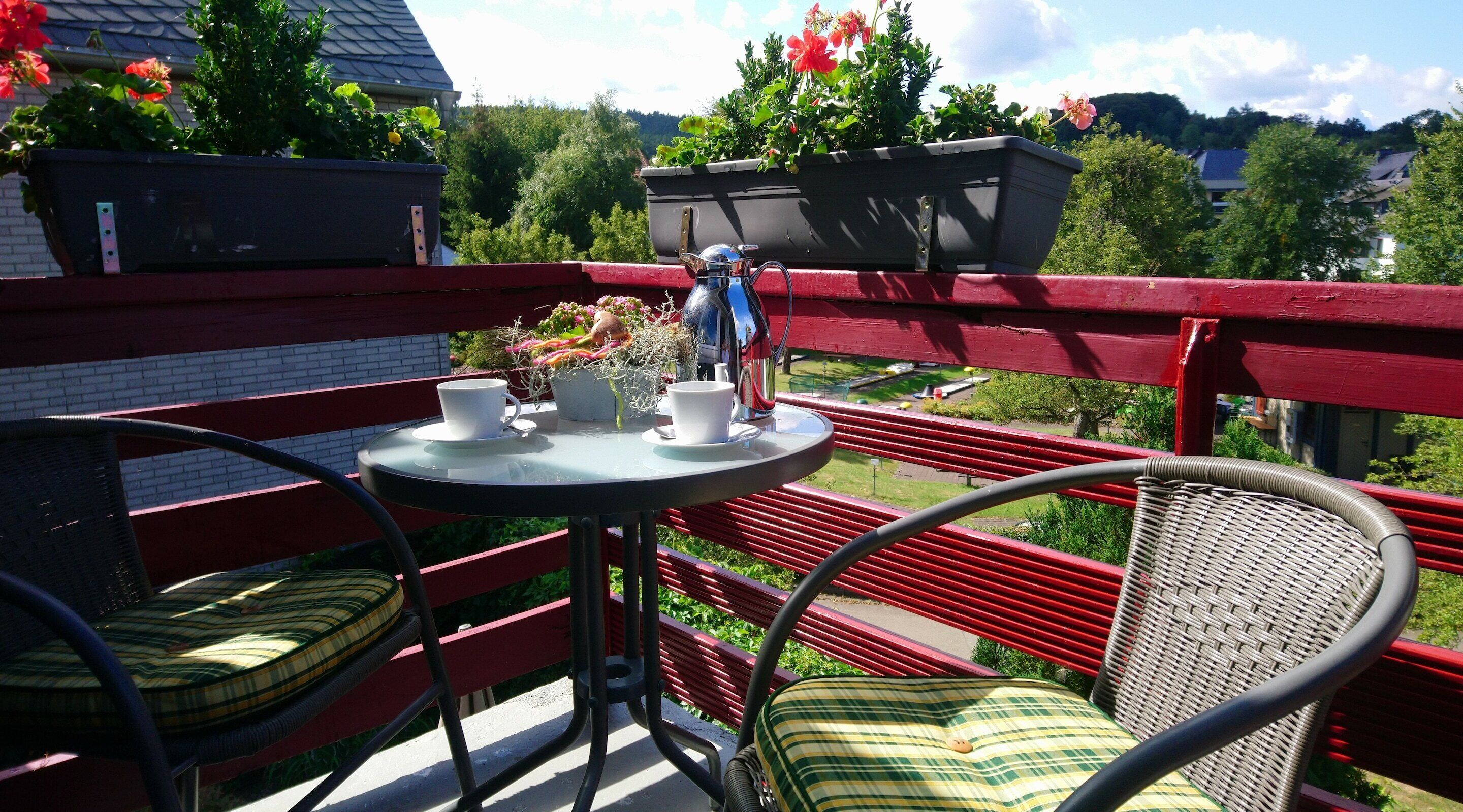 Un balcon avec une table ronde, deux chaises en osier et un pot de fleurs.