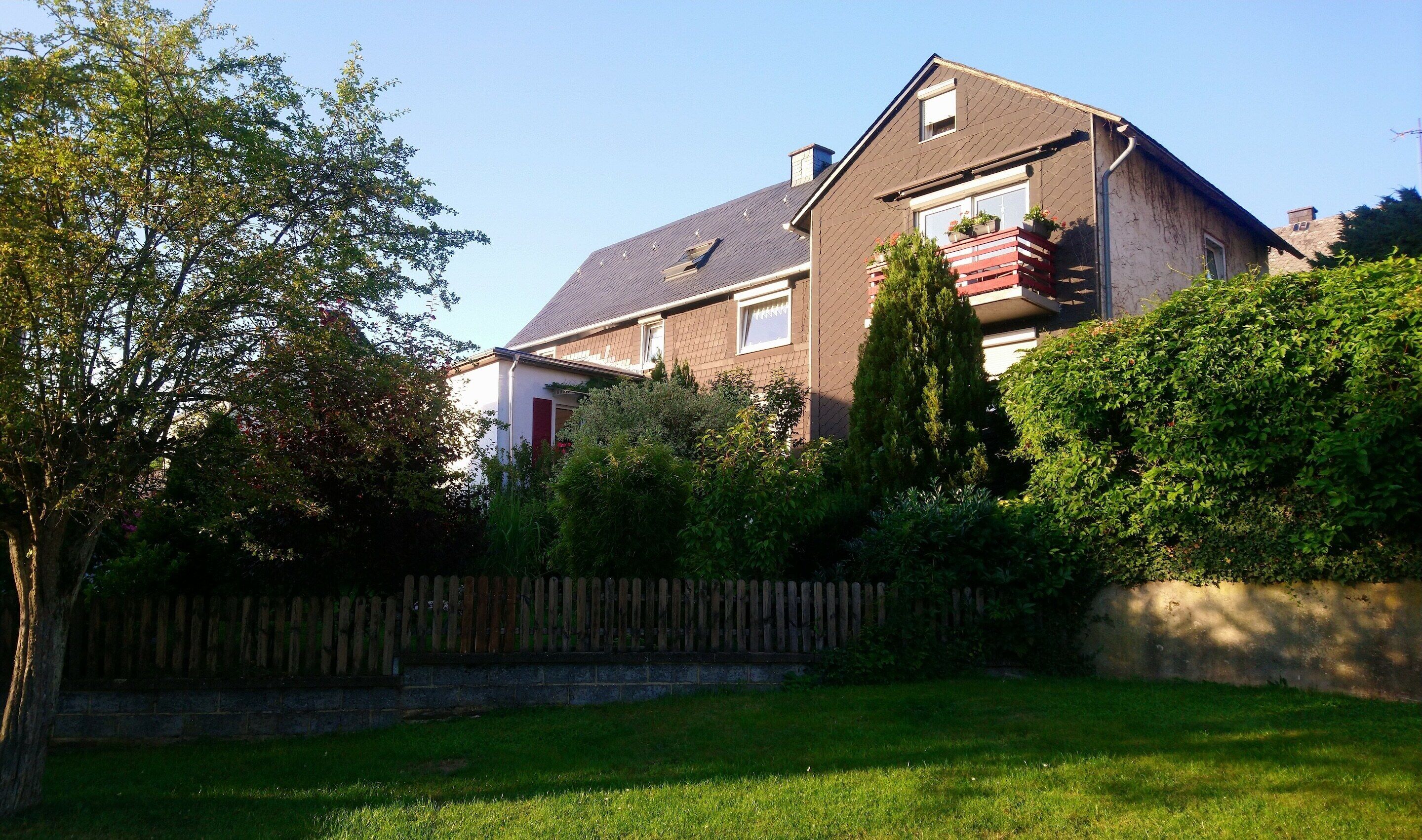 A two-story house with a sloped roof, a wooden fence, and a well-maintained lawn.