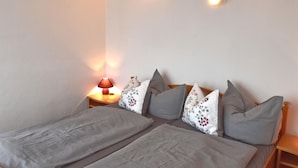 A bedroom with a bed, pillows, a nightstand, and a wall-mounted light fixture.