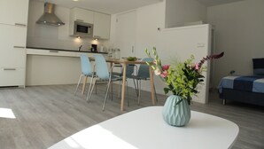 A modern kitchen with white cabinets, a microwave, and a dining area with a white table and blue chairs. - Stunning Apartment in Schoorl, North Holland, you can Bike to the Beach (Schoorl)