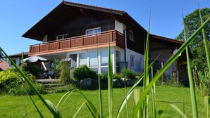 Ein zweistöckiges Haus mit Balkon, überdachter Terrasse und gepflegtem Rasen.