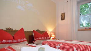 Ein Hotelzimmer mit zwei Betten, rot-weiß karierter Bettwäsche, einer Wand mit einem Wandgemälde mit dem Schriftzug 'Great Dreams', einer Nachttischlampe und einem Fenster mit Blick auf Bäume.