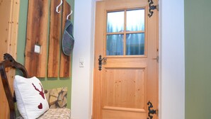 Eine Holztür mit Fenster, ein Stuhl mit floralem Kissen und ein Fellteppich auf dem Boden.