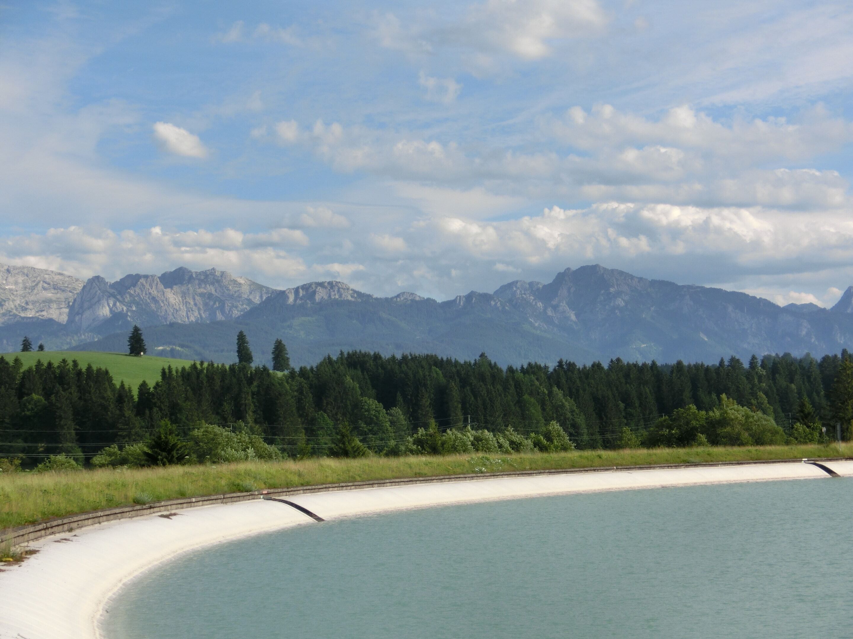 Un paysage côtier comprenant une plage de sable, une zone boisée et, au loin, une chaîne de montagnes.