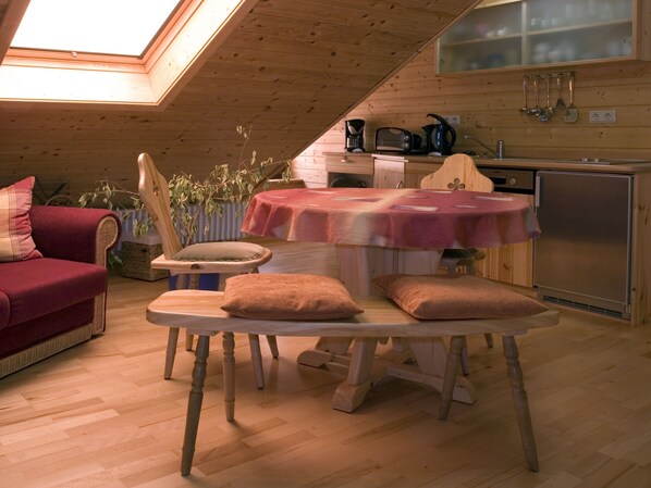 A cozy wooden cabin interior with a dining table, chairs, a sofa, and a kitchen area.