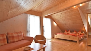 A cozy attic bedroom with a wooden ceiling, a bed with orange bedding, a sofa, and a chair. - Quaint Farmhouse in Langenbach near Lake (Schleusegrund)