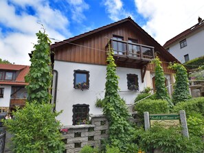Traditional chalet-style building with a balcony and lush greenery surroundings.