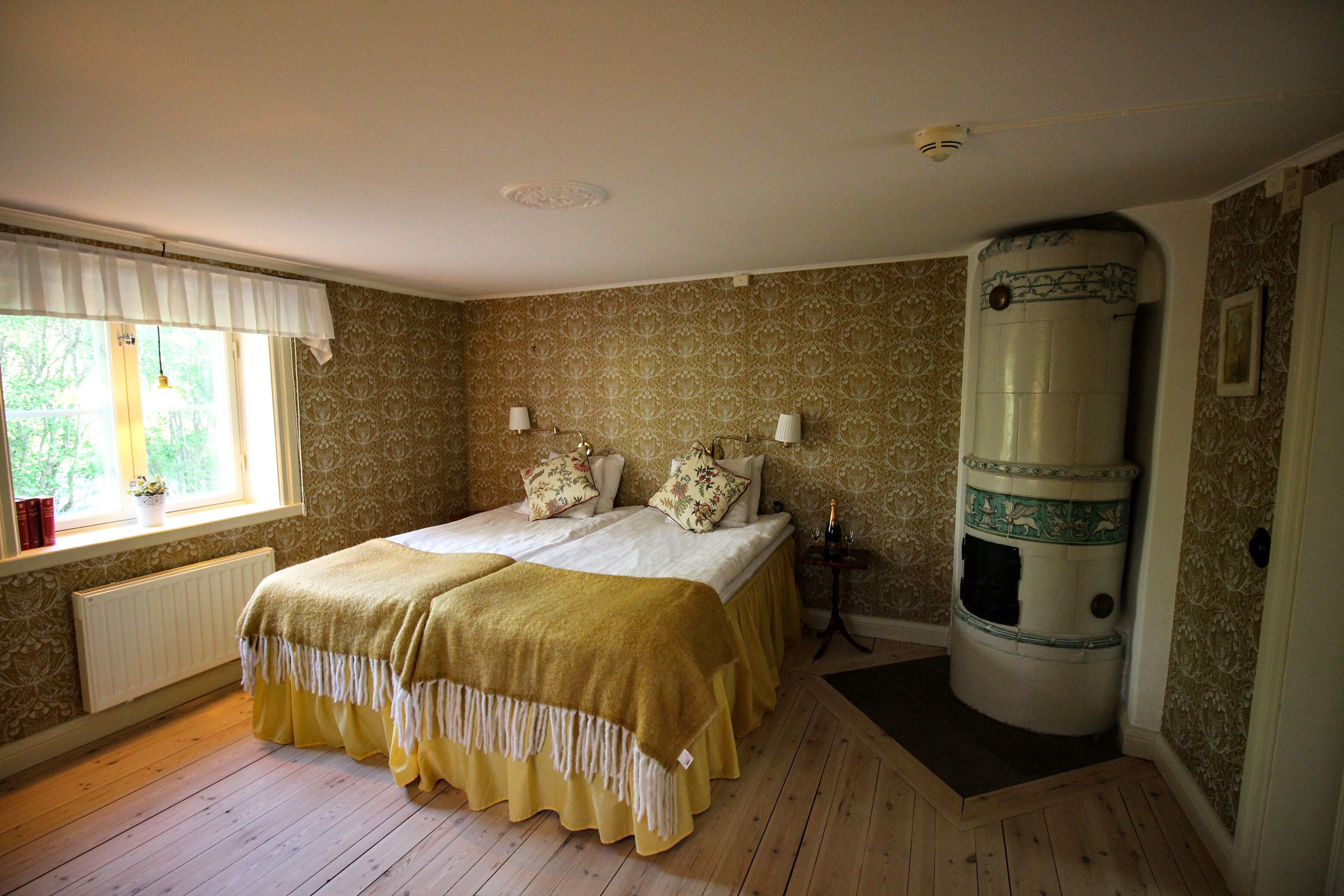 A bedroom with a double bed, two bedside lamps, a radiator, a window with a white valance, and a decorative column.