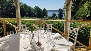 An outdoor dining area with a table set for six, surrounded by a wooden deck and overlooking a lake. - Riddersviks Herrgård (Hässelby)