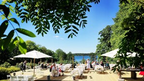 An outdoor dining area with tables and chairs, surrounded by greenery and a view of a lake. - Riddersviks Herrgård (Hässelby)