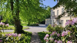 A pathway leading to a building surrounded by lush greenery and flowering shrubs. - Riddersviks Herrgård (Hässelby)