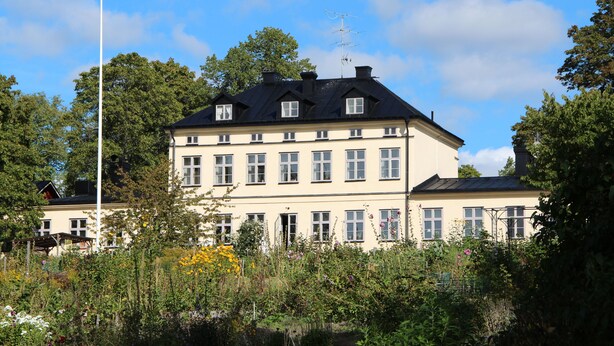 A large, multi-story building with a symmetrical facade, multiple windows, and a prominent chimney. - Riddersviks Herrgård (Hässelby)
