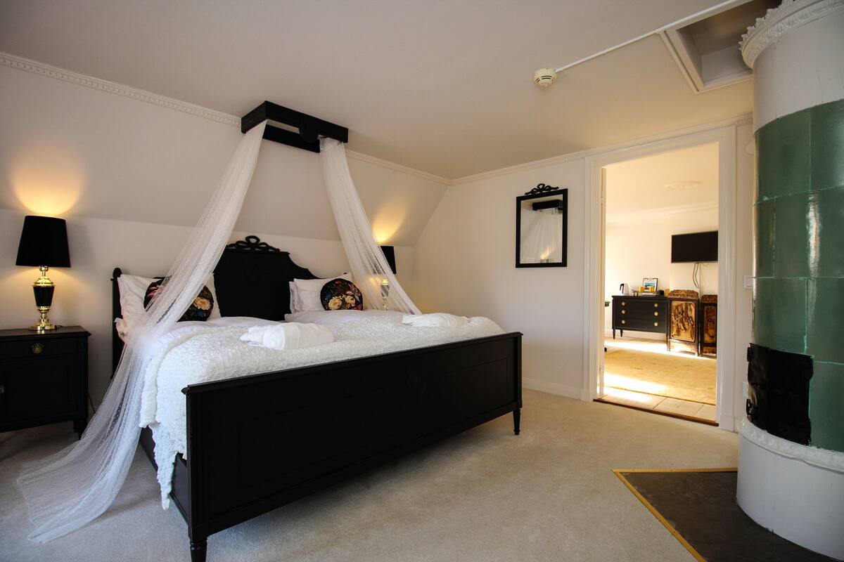 A bedroom with a four-poster bed, a nightstand with a lamp, and a green pillar.