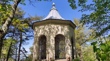 A stone gazebo with a pointed roof, surrounded by trees.