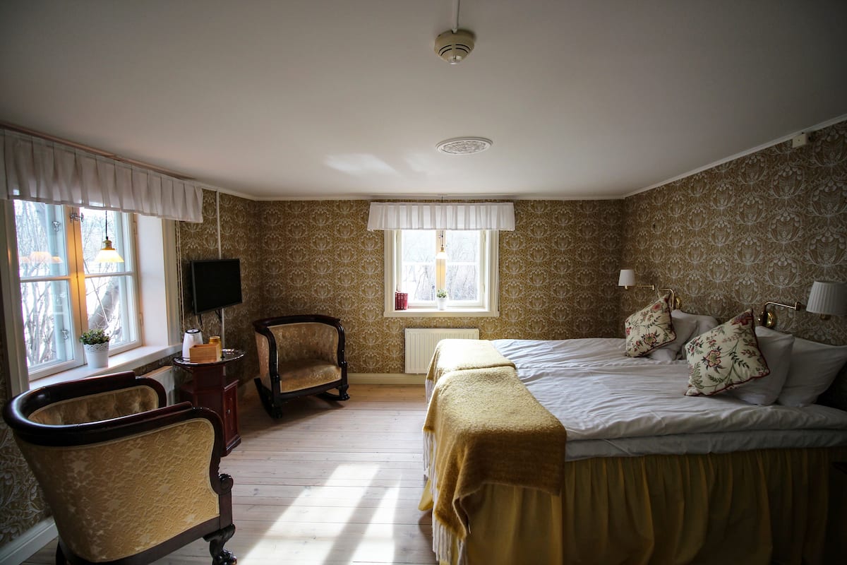 A bedroom with a bed, a chair, a television, and a window with curtains.