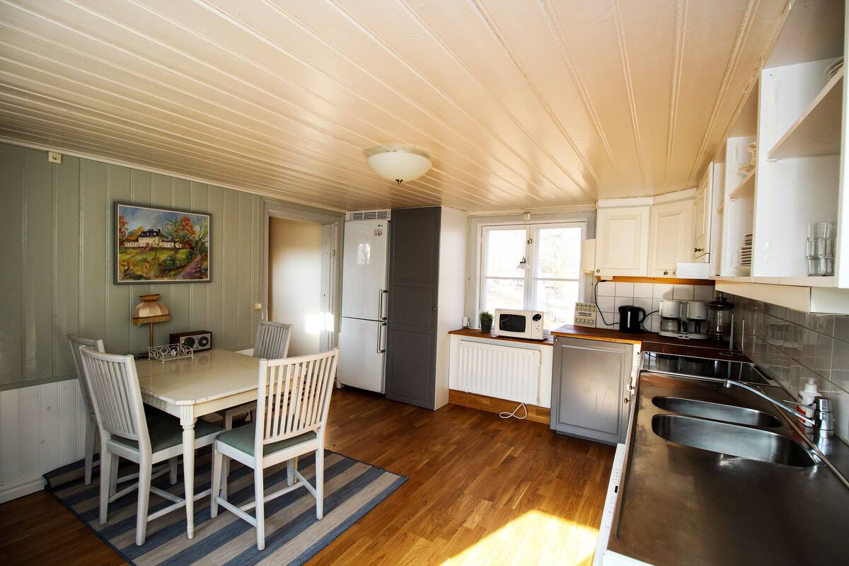 A compact kitchen with a dining area, featuring a refrigerator, microwave, sink, and wooden flooring.