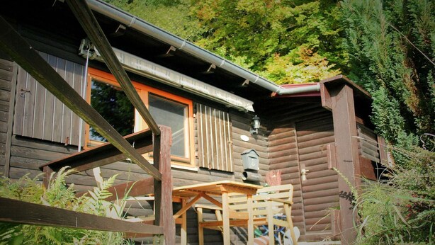 A rustic log cabin with a wooden deck and a table and chairs in front. - Holiday Home With Terrace (Stadlern)