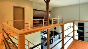 Um amplo loft com escada de madeira, um mezanino e vista para uma sala de estar com mobiliário.