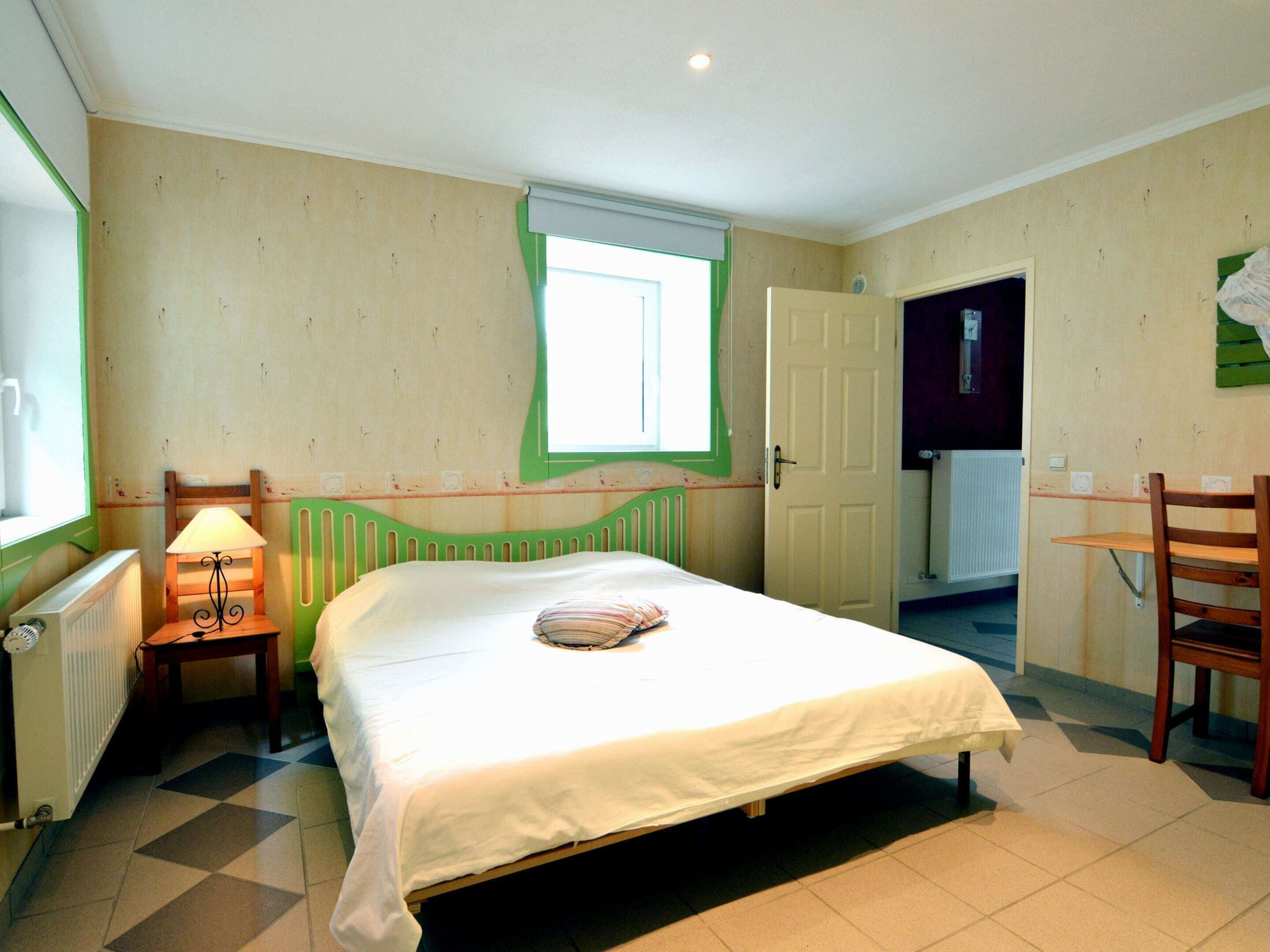 A bedroom with a single bed, a chair, a small table, a radiator, and a window.