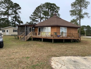 A wooden cabin with a deck, a covered porch, and a staircase leading to the entrance. - The Round House on Potato Creek at 1256 Quackenbush Road (Summerton)