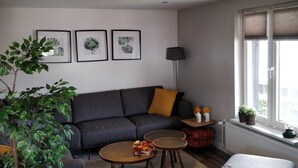 A living room with a grey sofa, a coffee table, a side table with two potted plants, and a floor lamp. There are three framed botanical prints on the wall. - Apartment in Eibergen Near Zwillbrocker Venn (Eibergen)
