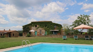A swimming pool with a stone building in the background, a grassy area, and a few lounge chairs. - Belvilla by Oyo Sorano (Sorano)
