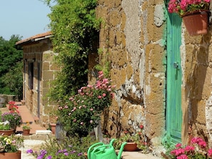 A rustic stone building with a green door, surrounded by potted plants and flowers. - Belvilla by Oyo Sorano (Sorano)
