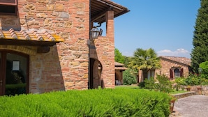 Un edificio in pietra con tetto in tegole, una porta di legno e un piccolo giardino con una palma.