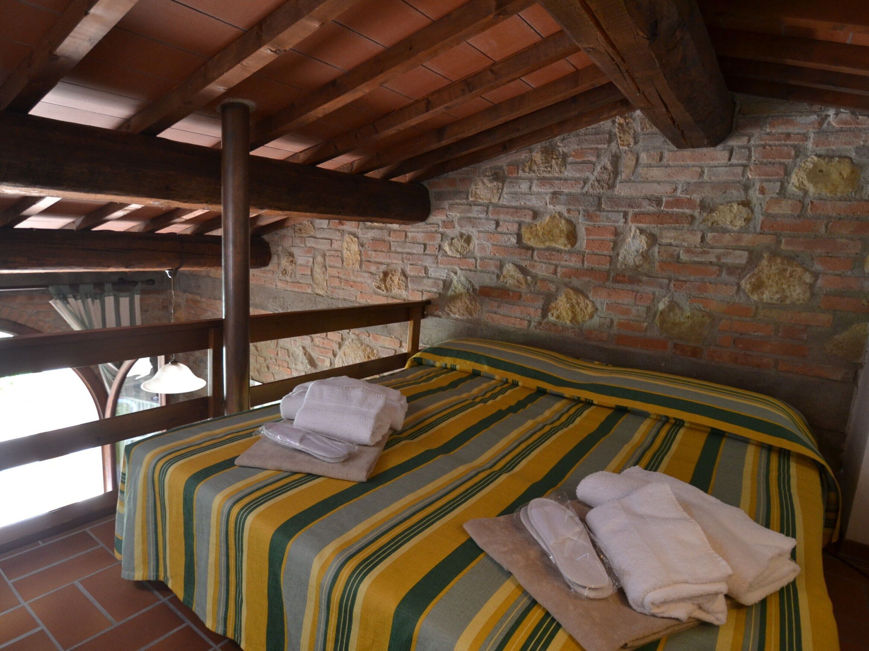 A room with a bed, wooden beams, brick walls, and a window.