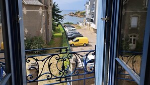 A coastal view from a balcony with a yellow car parked on the street, a row of parked cars, and buildings with stone facades. - Ancienne Gendarmerie With Sea Views (Clohars-Carnoët)