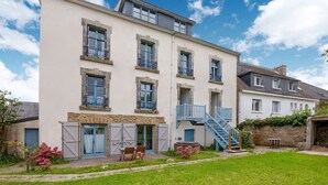 A multi-story building with a flat roof, a staircase leading to a balcony, and a small outdoor seating area. - Ancienne Gendarmerie With Sea Views (Clohars-Carnoët)