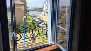A view from a window overlooking a coastal street with parked cars and buildings. - Ancienne Gendarmerie With Sea Views (Clohars-Carnoët)