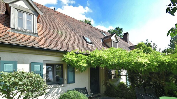 A house with a tiled roof, a small garden with a table and chairs, and a green door. - Superb Holiday Home in Weissenburg near Forest (Weissenburg in Bayern)