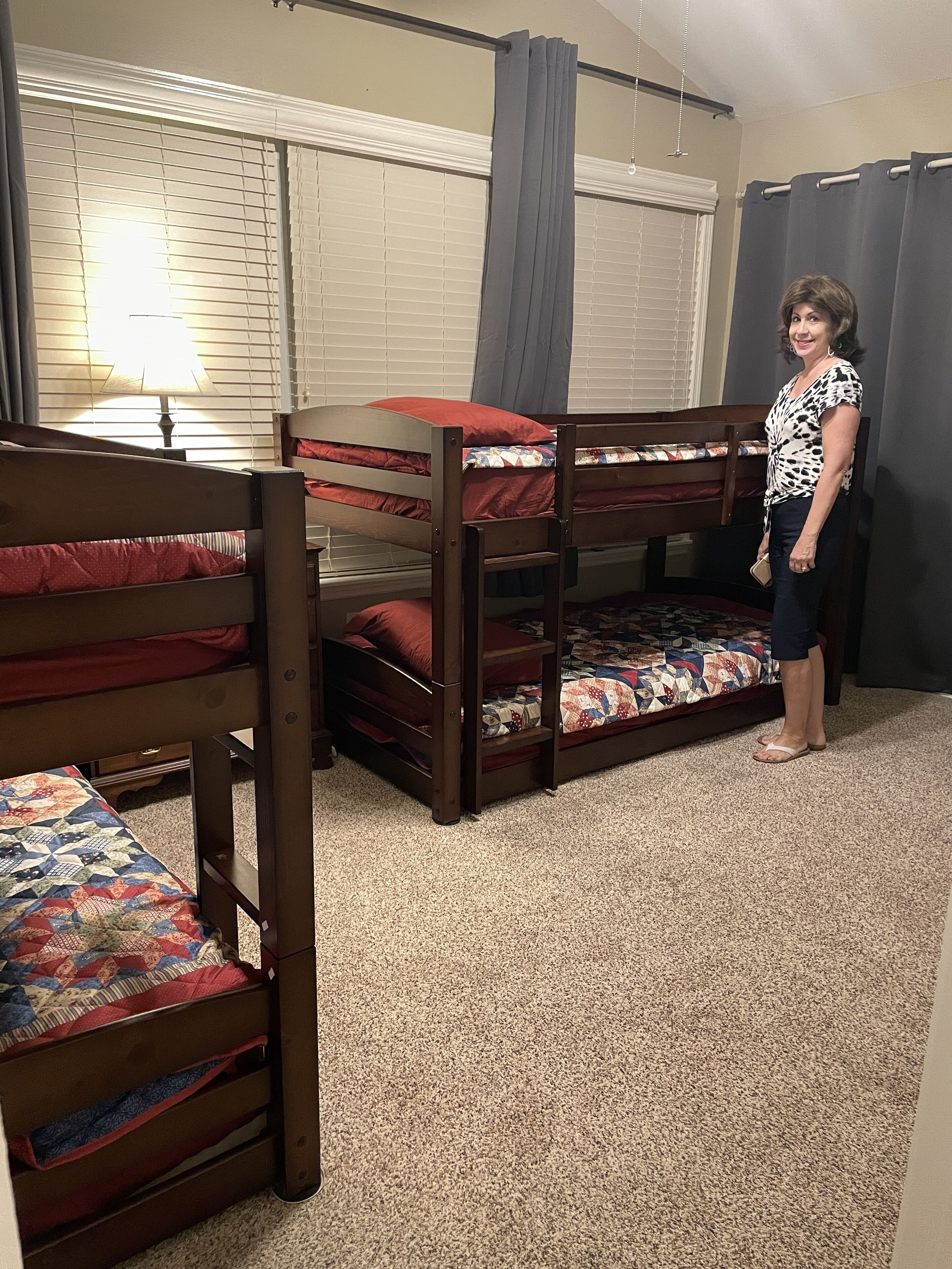 A room with bunk beds, a lamp, and a window with blinds.