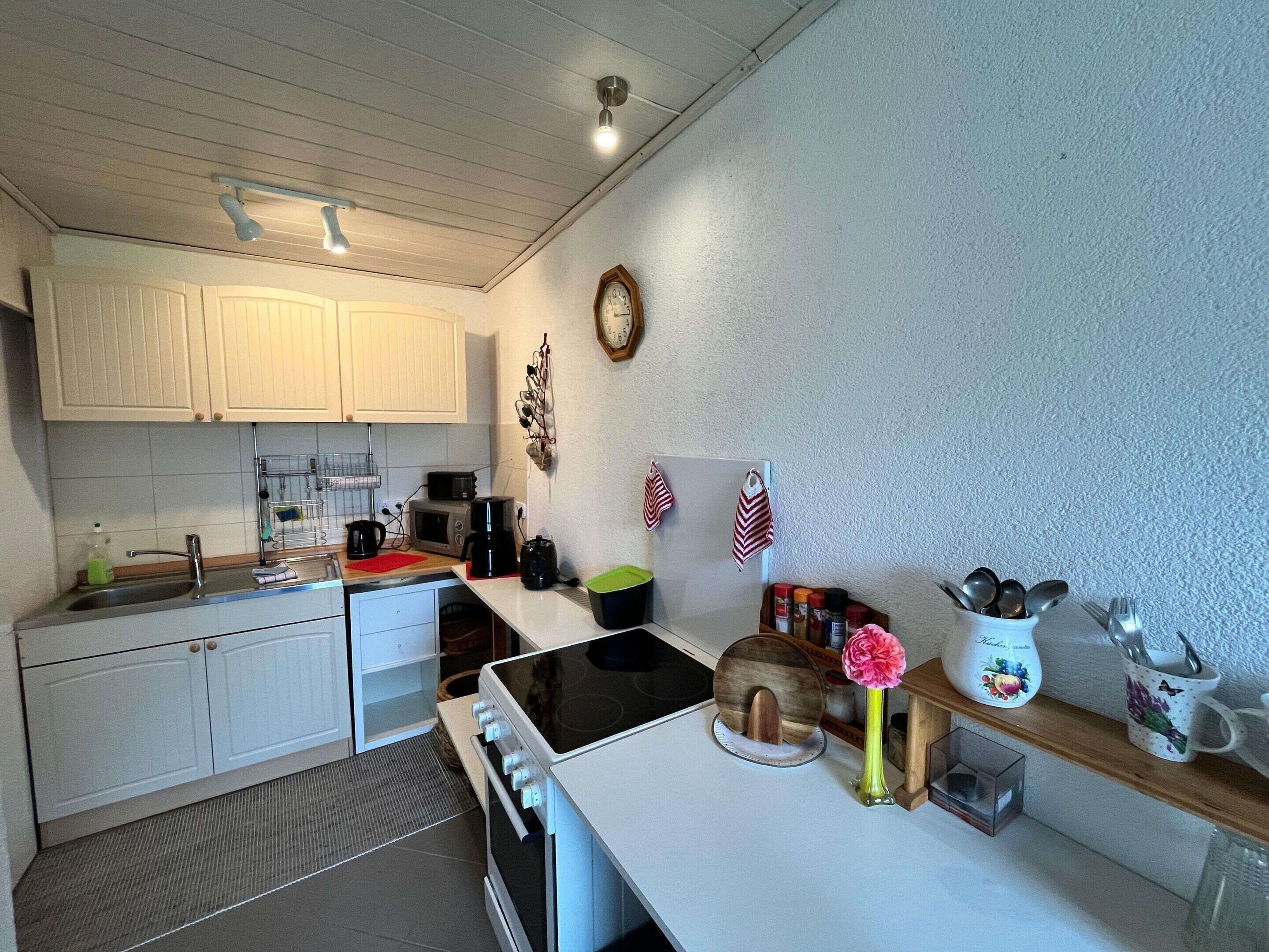A kitchen with white cabinets, a microwave, a stove, a sink, and various kitchen items on the counter.