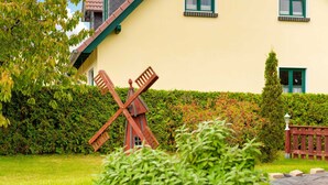 Un jardin bien entretenu, agrémenté d’une sculpture de moulin à vent, de haies taillées avec soin et d’une maison aux volets verts.