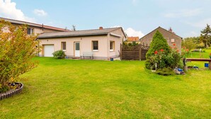 Une maison à deux étages avec un jardin devant et un petit potager.