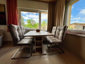 Ein Essbereich mit Tisch und Stühlen, ein Fenster mit Vorhängen und Blick auf Bäume und einen Basketballkorb.