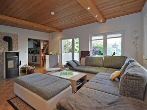 A cozy living room with a sofa, a coffee table, and a fireplace. There is a kitchen area with cabinets and a window. - Holiday Home in Gntersberge With Garden (Harzgerode)