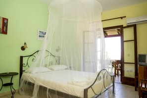 A room with a bed under a mosquito net, a small table, a television, and an air conditioning unit. - Studios Petra (Zakynthos)