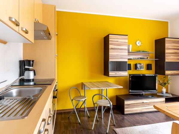 A compact kitchen with a coffee maker, two foldable chairs, a TV, and wooden cabinets. - Ferienwohnung in der Nahe von Wismar (Wismar)