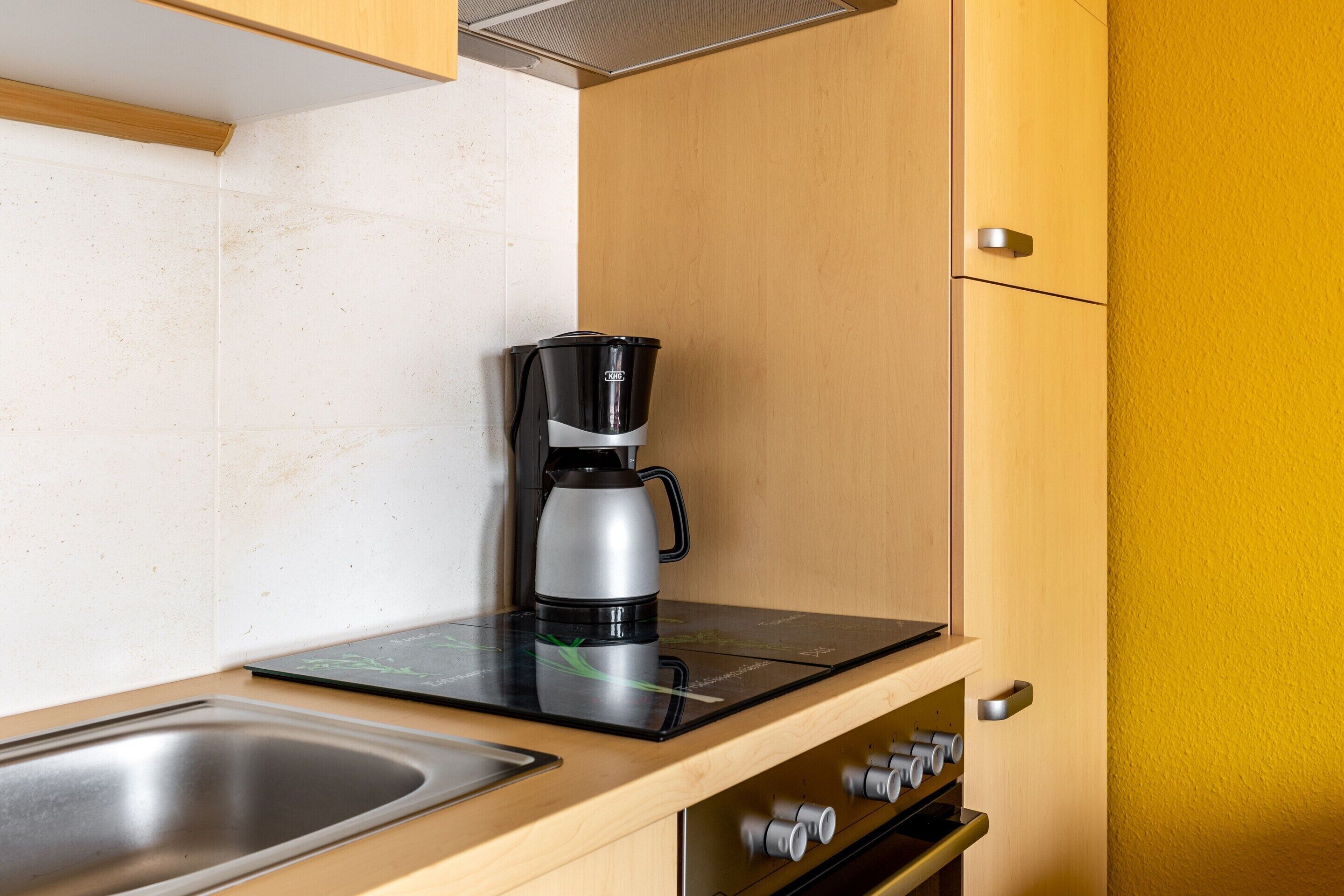 A kitchen with a coffee maker on a black countertop, a stainless steel sink, and wooden cabinets.