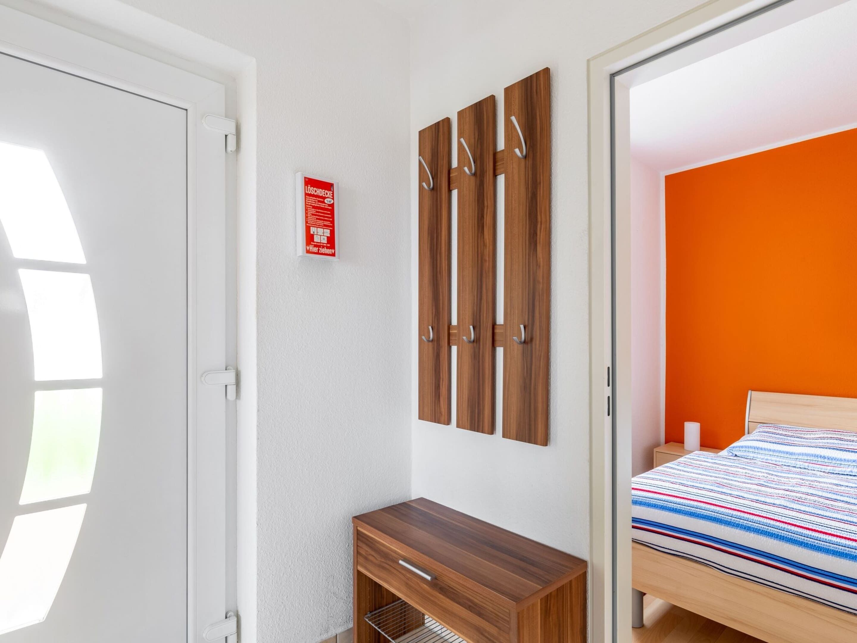 A bedroom with a wooden wardrobe, a bed with a striped blanket, and a red fire safety sign on the wall.