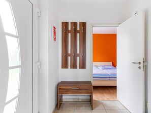 A bedroom with a bed, a wooden bench, a wall-mounted shelf, and a door with a sign.